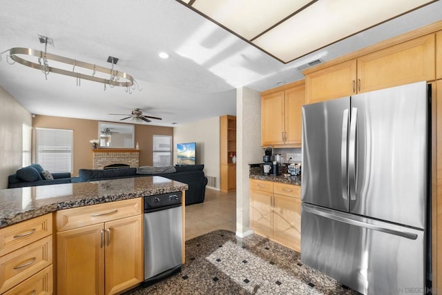 kitchen featuring a brick fireplace, light brown cabinets, stainless steel fridge, and dark stone counters