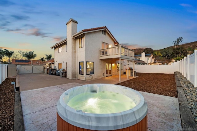 back house at dusk with a balcony, a patio, and a hot tub