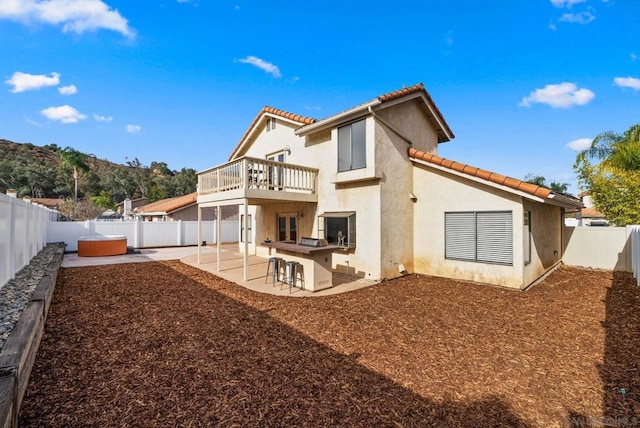 back of property featuring a balcony, a patio area, exterior bar, and a hot tub