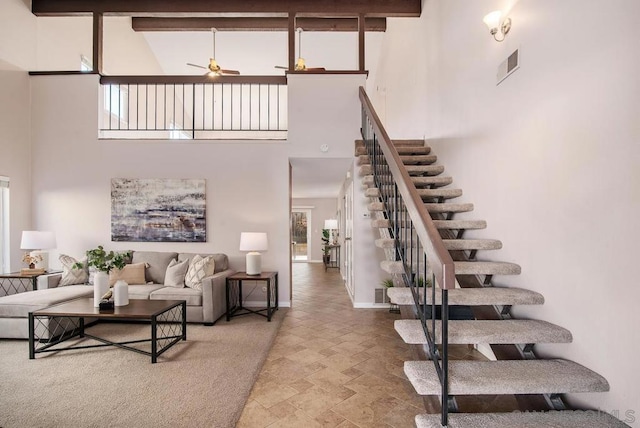 stairs with ceiling fan, beamed ceiling, and a high ceiling