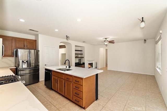 kitchen featuring built in shelves, sink, a center island with sink, stainless steel fridge, and black dishwasher