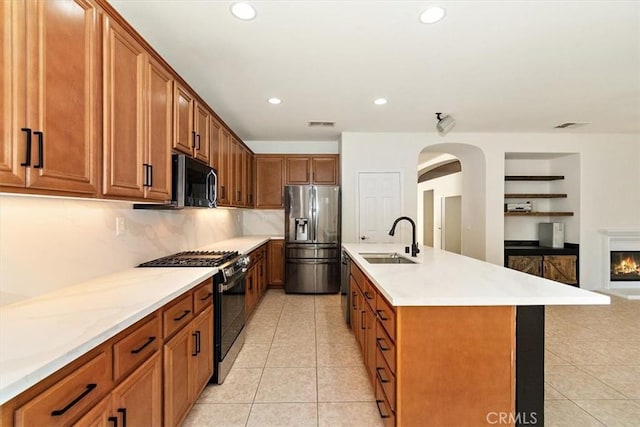 kitchen featuring light tile patterned flooring, sink, decorative backsplash, stainless steel appliances, and a center island with sink