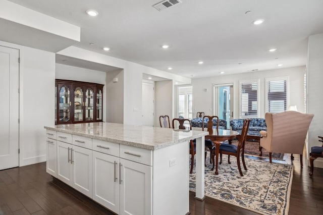 kitchen with white cabinetry, a kitchen breakfast bar, light stone counters, a kitchen island, and dark hardwood / wood-style flooring