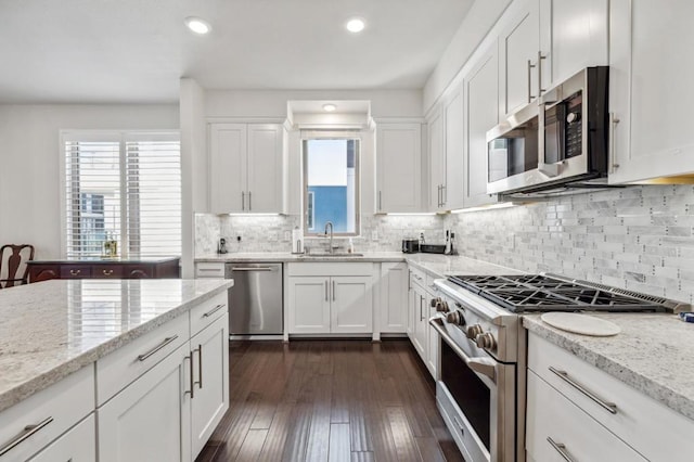 kitchen with sink, dark wood-type flooring, appliances with stainless steel finishes, light stone counters, and white cabinets