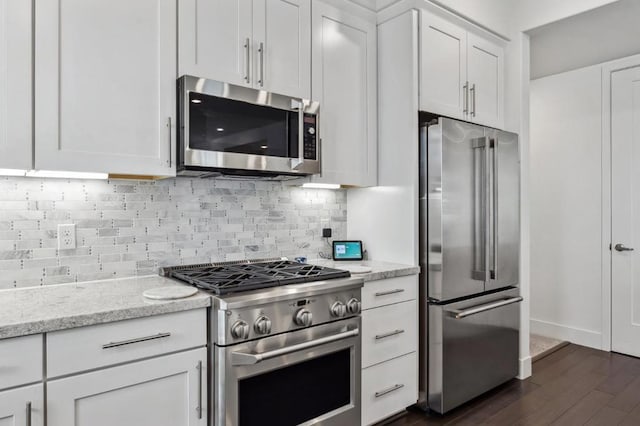 kitchen featuring appliances with stainless steel finishes, white cabinetry, backsplash, light stone countertops, and dark hardwood / wood-style flooring