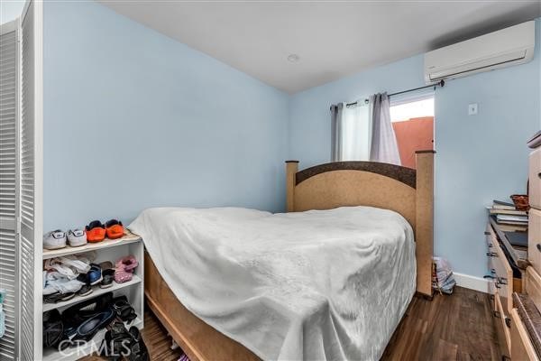 bedroom with an AC wall unit and dark wood-type flooring