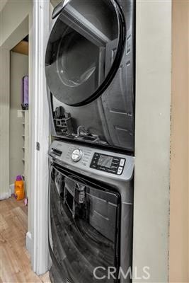 clothes washing area with light hardwood / wood-style floors and stacked washer / drying machine