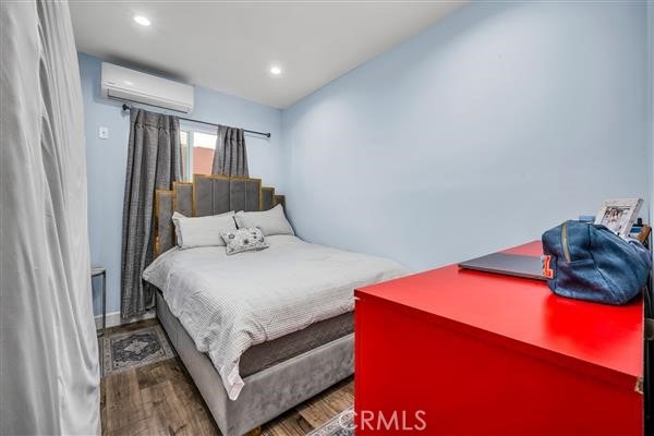 bedroom featuring hardwood / wood-style flooring and a wall unit AC