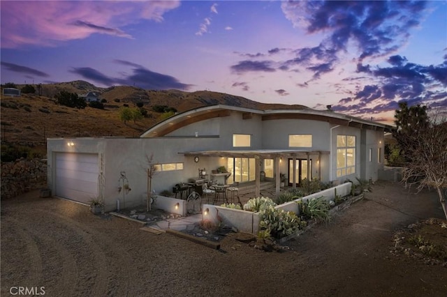 back house at dusk with a mountain view, a patio area, and a garage