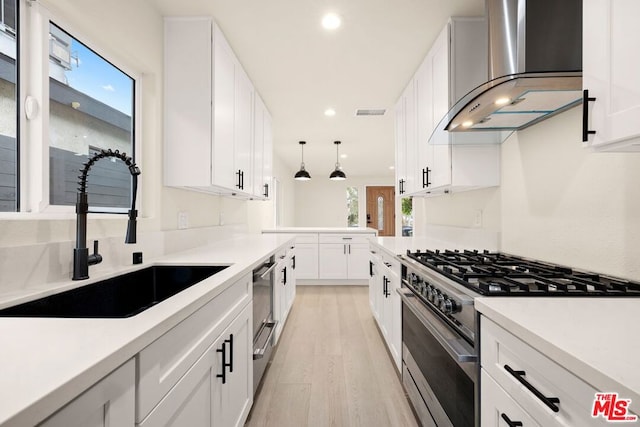 kitchen featuring high end stainless steel range oven, sink, wall chimney range hood, and white cabinets