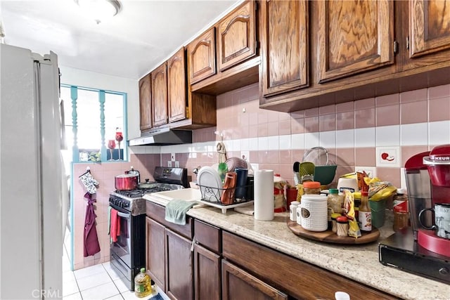 kitchen with light stone counters, fridge, light tile patterned floors, and stainless steel range with gas stovetop