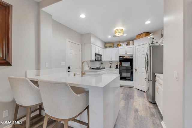 kitchen featuring black appliances, kitchen peninsula, white cabinetry, and a kitchen bar