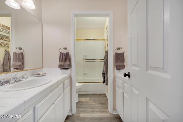 full bathroom featuring wood-type flooring, shower / bath combination with glass door, vanity, and toilet