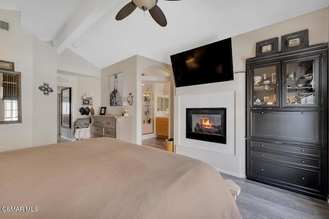 bedroom with ceiling fan, lofted ceiling with beams, a fireplace, hardwood / wood-style floors, and connected bathroom