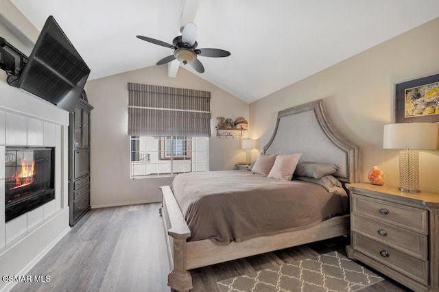 bedroom featuring a tiled fireplace, dark hardwood / wood-style floors, vaulted ceiling, and ceiling fan