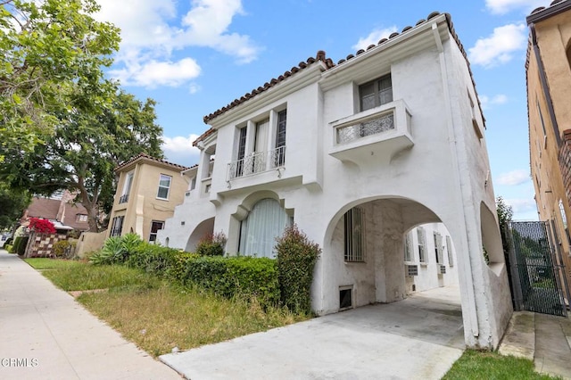 mediterranean / spanish house featuring a tile roof, fence, a balcony, and stucco siding