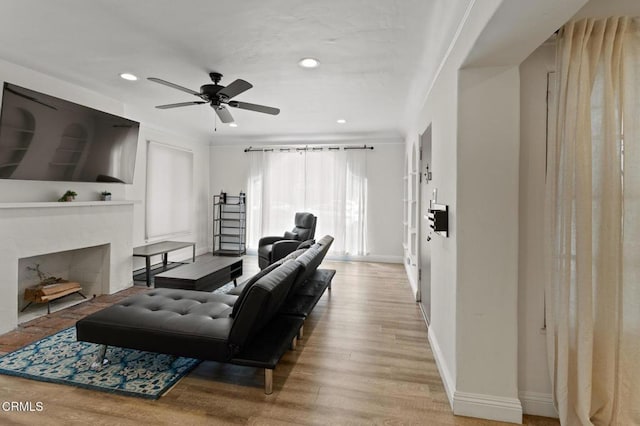 living room featuring a fireplace with flush hearth, wood finished floors, baseboards, recessed lighting, and a ceiling fan