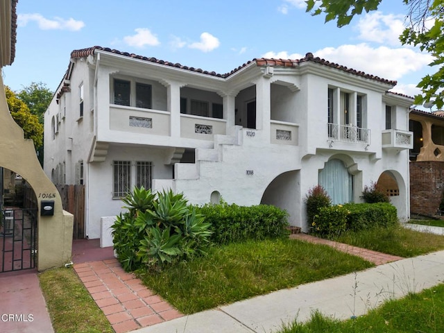 mediterranean / spanish house featuring a tiled roof, stucco siding, a balcony, and fence