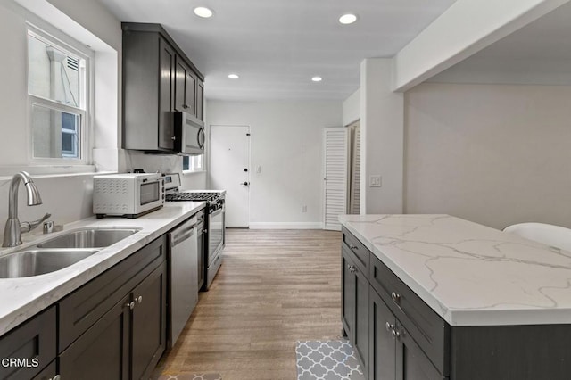 kitchen featuring light stone countertops, recessed lighting, a sink, light wood finished floors, and stainless steel appliances