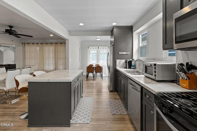 kitchen with ceiling fan, a sink, light stone counters, light wood-style floors, and stainless steel appliances