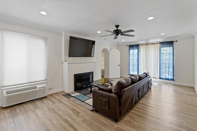 living room featuring light wood-style floors, an AC wall unit, arched walkways, recessed lighting, and baseboards