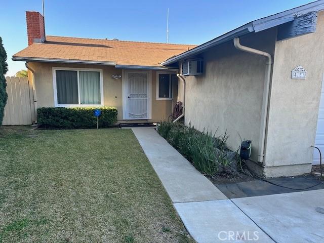 property entrance featuring a yard, fence, a chimney, and stucco siding