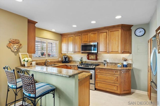 kitchen with kitchen peninsula, a kitchen breakfast bar, appliances with stainless steel finishes, sink, and light stone counters