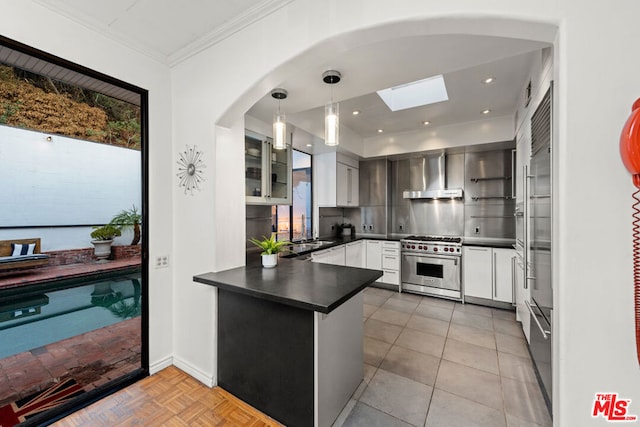 kitchen featuring pendant lighting, white cabinetry, high end stainless steel range oven, a skylight, and wall chimney range hood