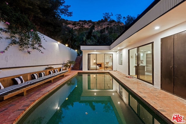 pool at dusk featuring a mountain view and a patio