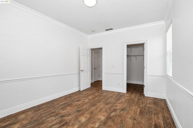 unfurnished bedroom with ornamental molding, dark wood-type flooring, a closet, and a walk in closet