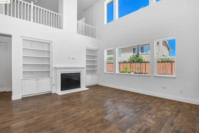 unfurnished living room with built in features, a towering ceiling, and dark hardwood / wood-style flooring