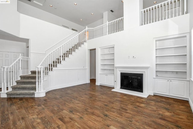 unfurnished living room featuring built in features, a towering ceiling, and dark hardwood / wood-style flooring