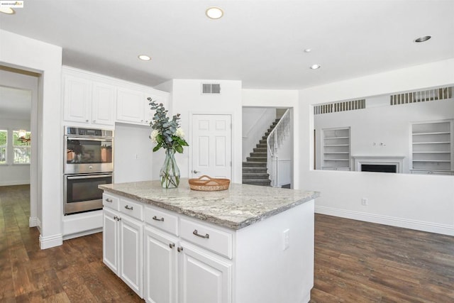 kitchen featuring a center island, white cabinetry, built in shelves, light stone counters, and double oven