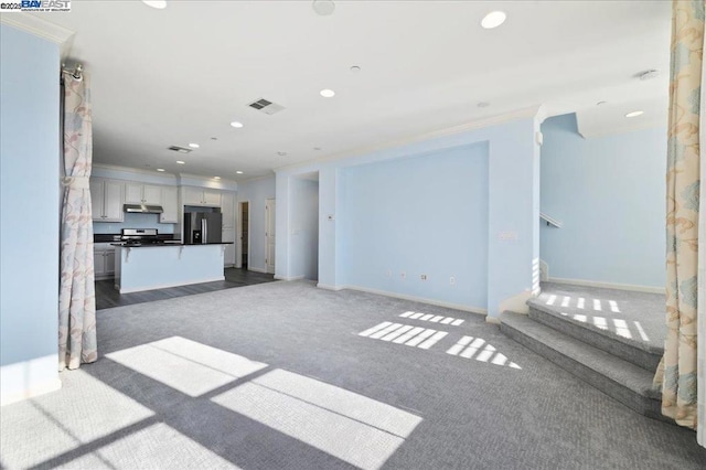 unfurnished living room featuring dark colored carpet and ornamental molding