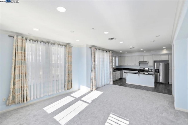 kitchen with crown molding, appliances with stainless steel finishes, white cabinetry, dark carpet, and a kitchen island