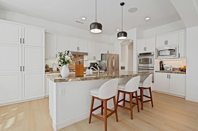 kitchen featuring stainless steel appliances, stone countertops, a kitchen island with sink, and white cabinets