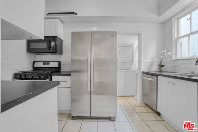 kitchen featuring sink, backsplash, white cabinets, stacked washing maching and dryer, and stainless steel appliances