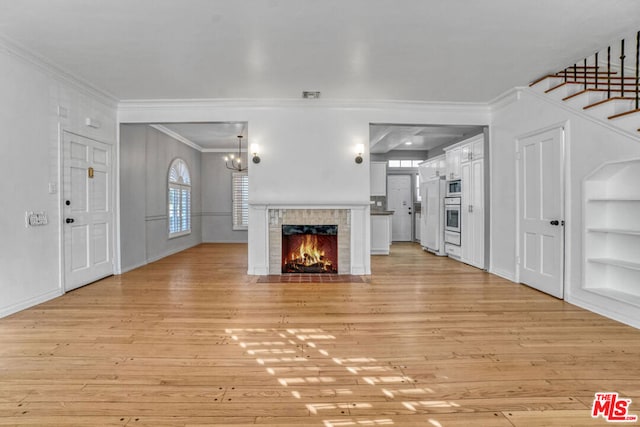 unfurnished living room featuring light hardwood / wood-style floors, built in features, ornamental molding, and a notable chandelier