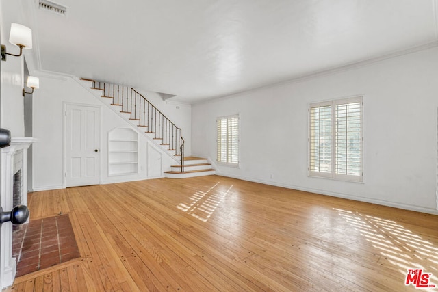 unfurnished living room featuring built in shelves, crown molding, and light wood-type flooring