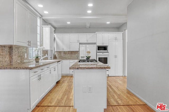 kitchen with a kitchen island, white appliances, white cabinets, and light stone countertops