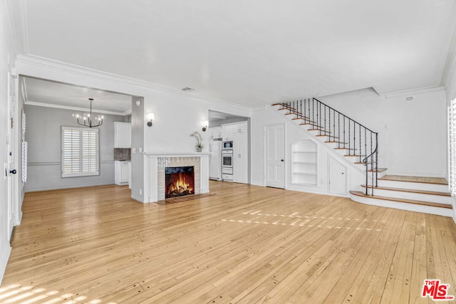 unfurnished living room featuring built in shelves, light hardwood / wood-style floors, a fireplace, and crown molding