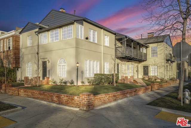 property exterior at dusk with a balcony and a yard