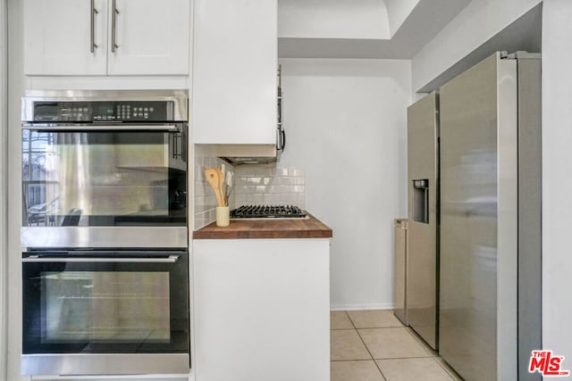 kitchen featuring tasteful backsplash, white cabinetry, butcher block countertops, light tile patterned flooring, and stainless steel appliances