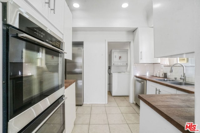 kitchen featuring stacked washer / dryer, white cabinets, butcher block counters, stainless steel appliances, and sink