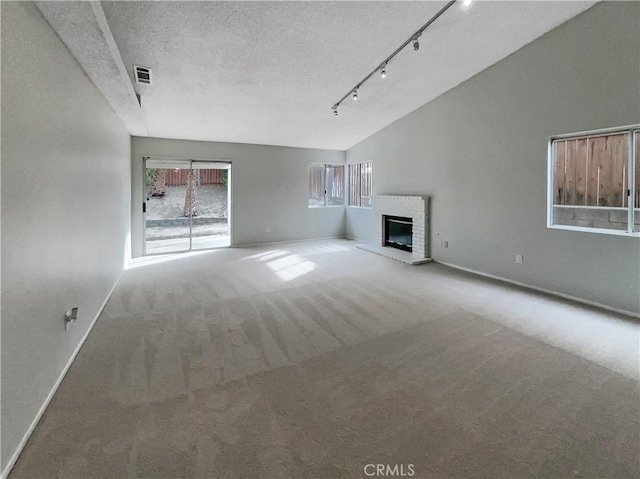 unfurnished living room featuring vaulted ceiling, a fireplace, carpet flooring, track lighting, and a textured ceiling