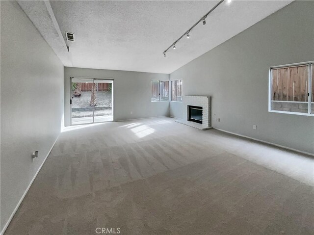 unfurnished living room featuring rail lighting, vaulted ceiling, a brick fireplace, a textured ceiling, and carpet floors