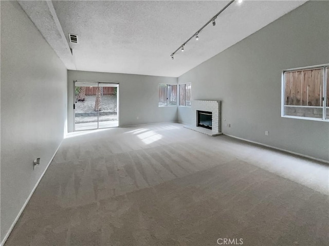 unfurnished living room featuring a fireplace, carpet floors, vaulted ceiling, track lighting, and a textured ceiling