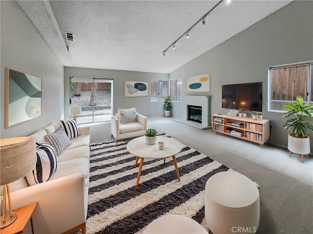 living room featuring vaulted ceiling, a fireplace, rail lighting, carpet floors, and a textured ceiling