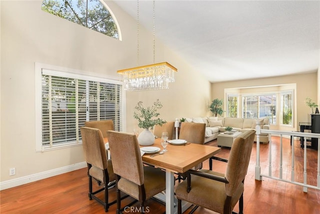 dining space with wood-type flooring, lofted ceiling, and an inviting chandelier