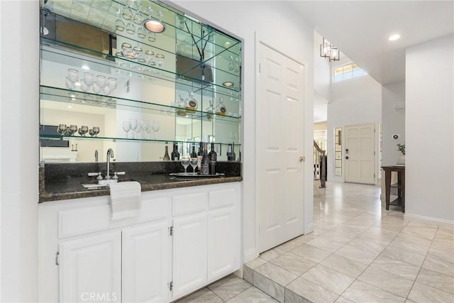 bar with sink, dark stone counters, white cabinets, and a high ceiling